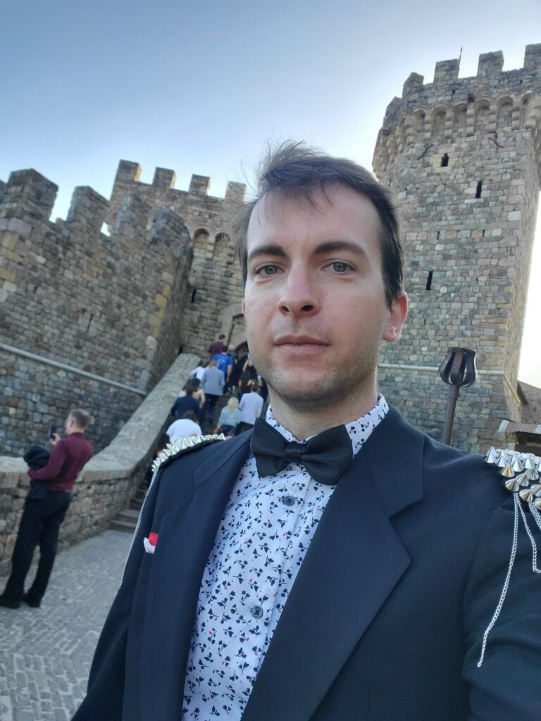 Me, Ethan, outside the Italian castle, wearing a black tuxedo, bowtie, nice shirt, pocket square, and spiky chain epaulets.